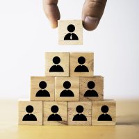 Hand putting manager icon on top of wooden stacking of staff icons for promotion leadership and teamwork concept.